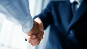 Close-up photograph of corporate handshake between two professionals in business suits with soft focus background, representing trust, cooperation and formal business agreement
